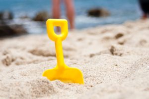 Small yellow shovel stuck in the sand with water in background