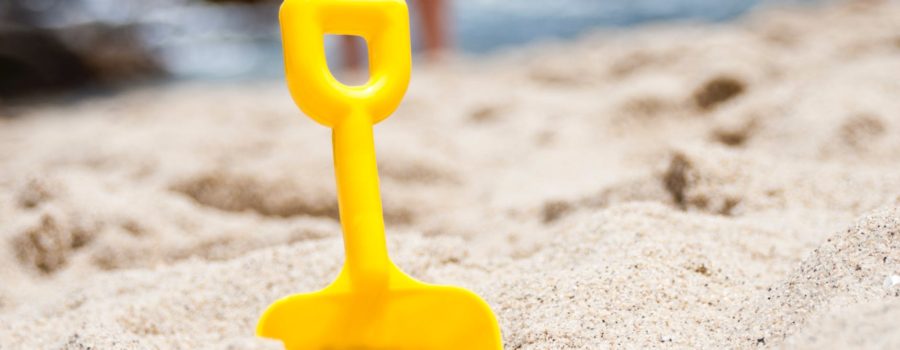 Small yellow shovel stuck in the sand with water in background