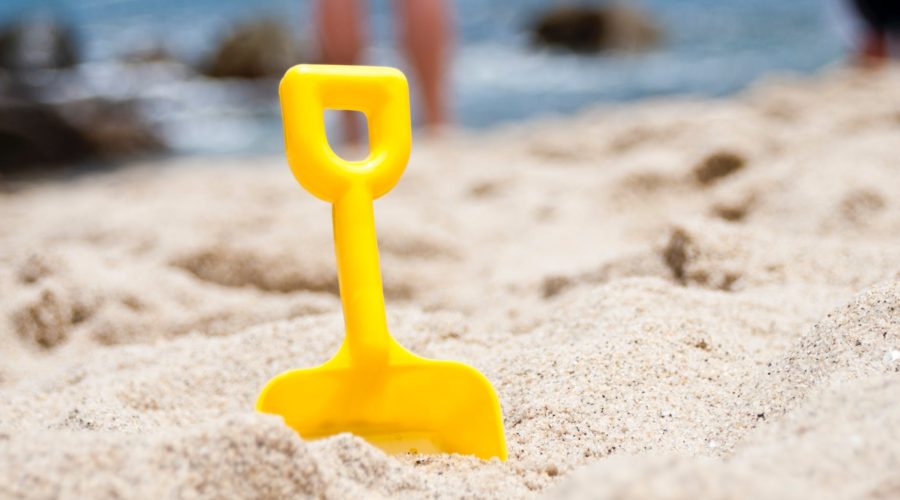 Small yellow shovel stuck in the sand with water in background